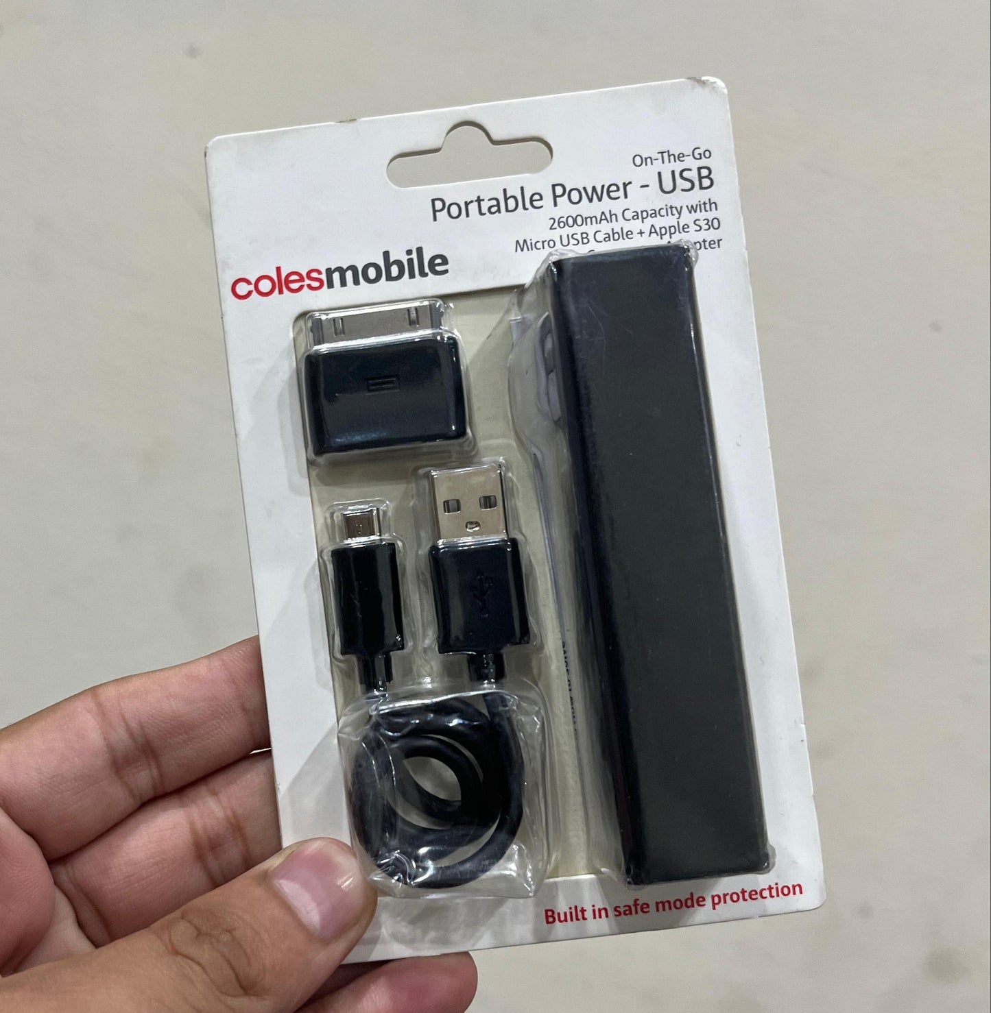 Hand holding a Coles Mobile portable power USB device packaging on a light gray background